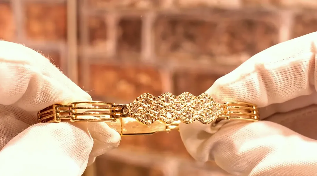 Colin’s handmade gold bracelet, set with diamonds, held in white cotton gloves
