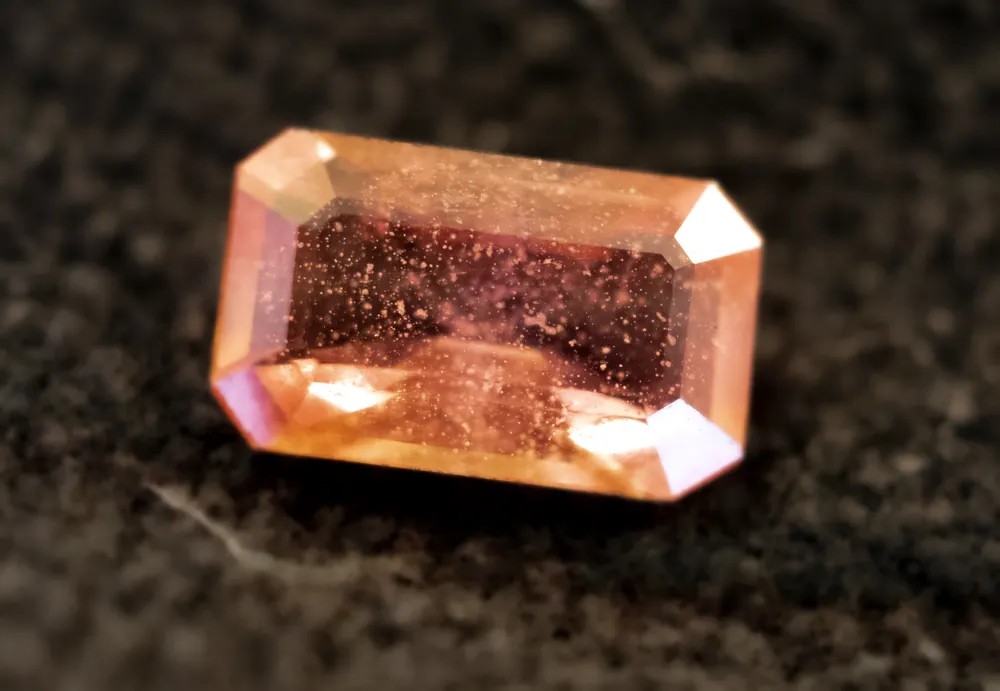 A loose padparadscha sapphire, emerald cut, on dark velvet