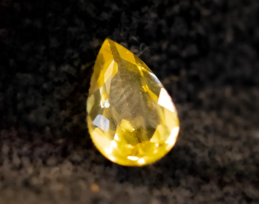 A loose pear-shaped yellow sapphire on dark velvet